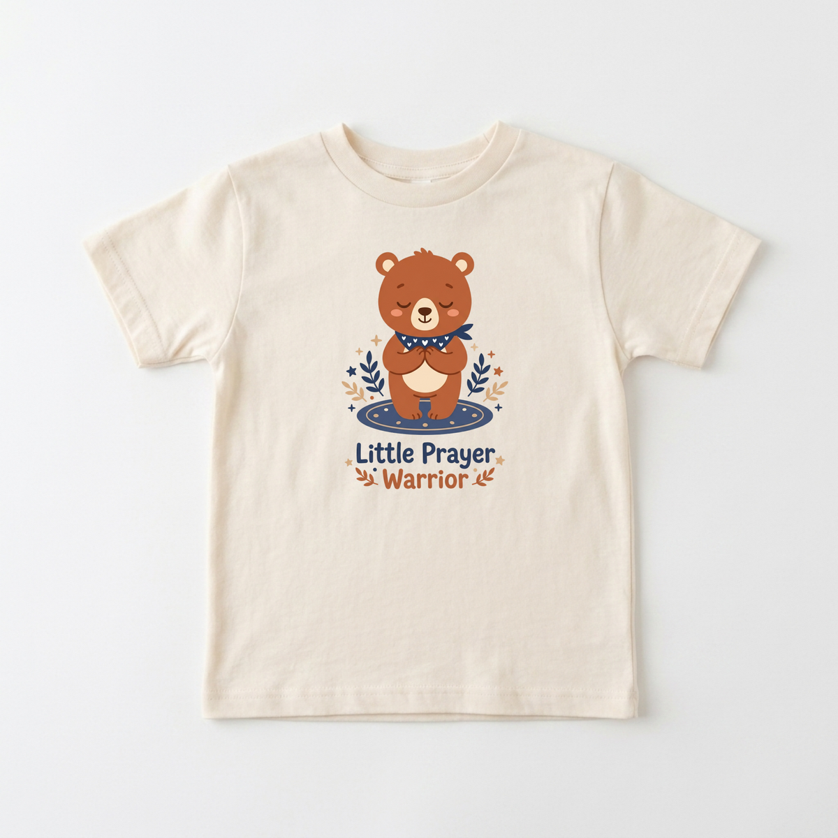 The Little Prayer Warrior Bear Toddler Shirt – Faith Tee by Toodleroos features a beige design with an illustrated brown bear with closed eyes, paws together in prayer, surrounded by leaves, and the words “Little Prayer Warrior” underneath. This sweet toddler shirt makes a perfect baptism gift or addition to any collection of Christian kids shirts.