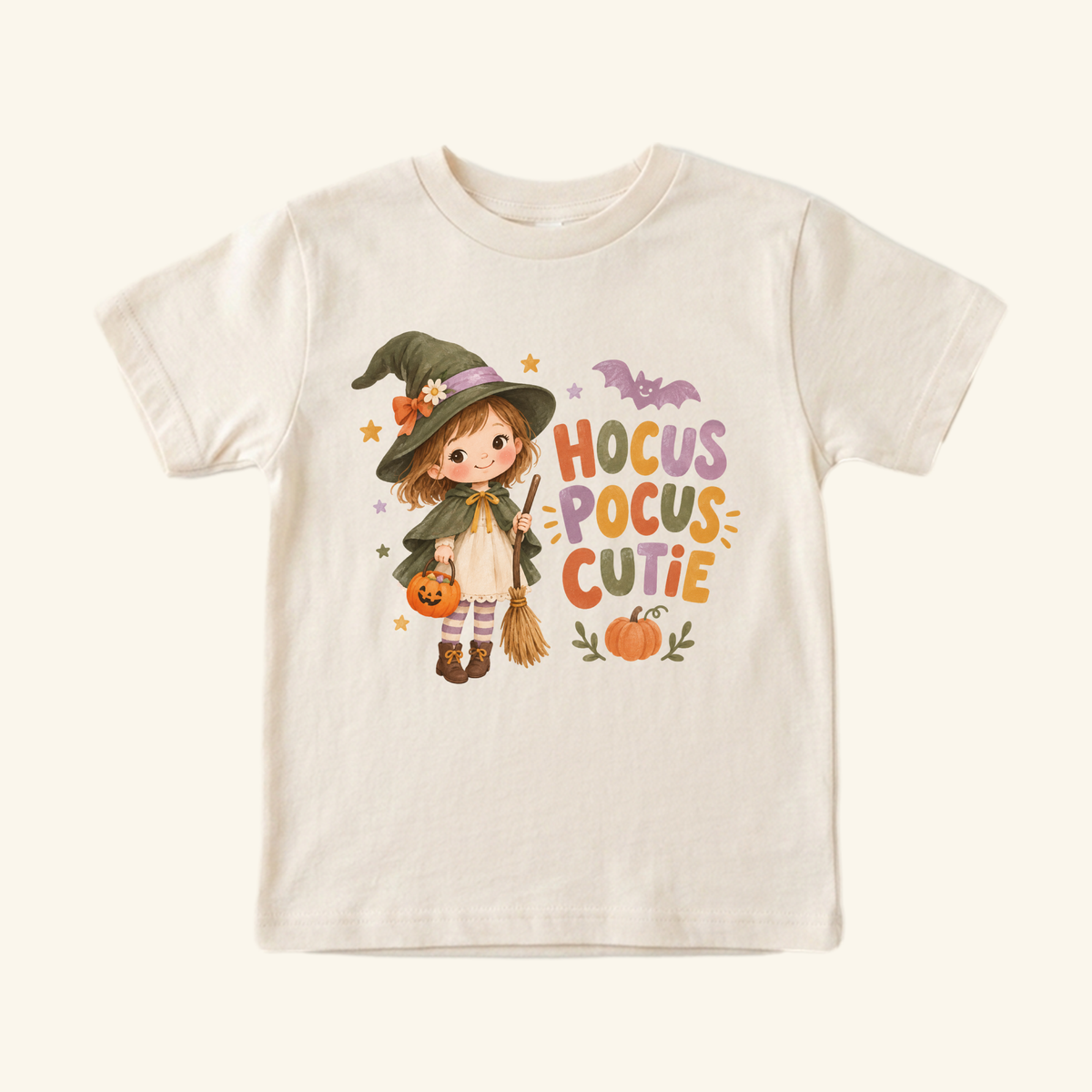 A cream Toodleroos Hocus Pocus Cutie Witch Toddler Halloween Shirt featuring a cartoon girl dressed as a cute witch holding a pumpkin bucket and broom, with the text Hocus Pocus Cutie and a small bat.