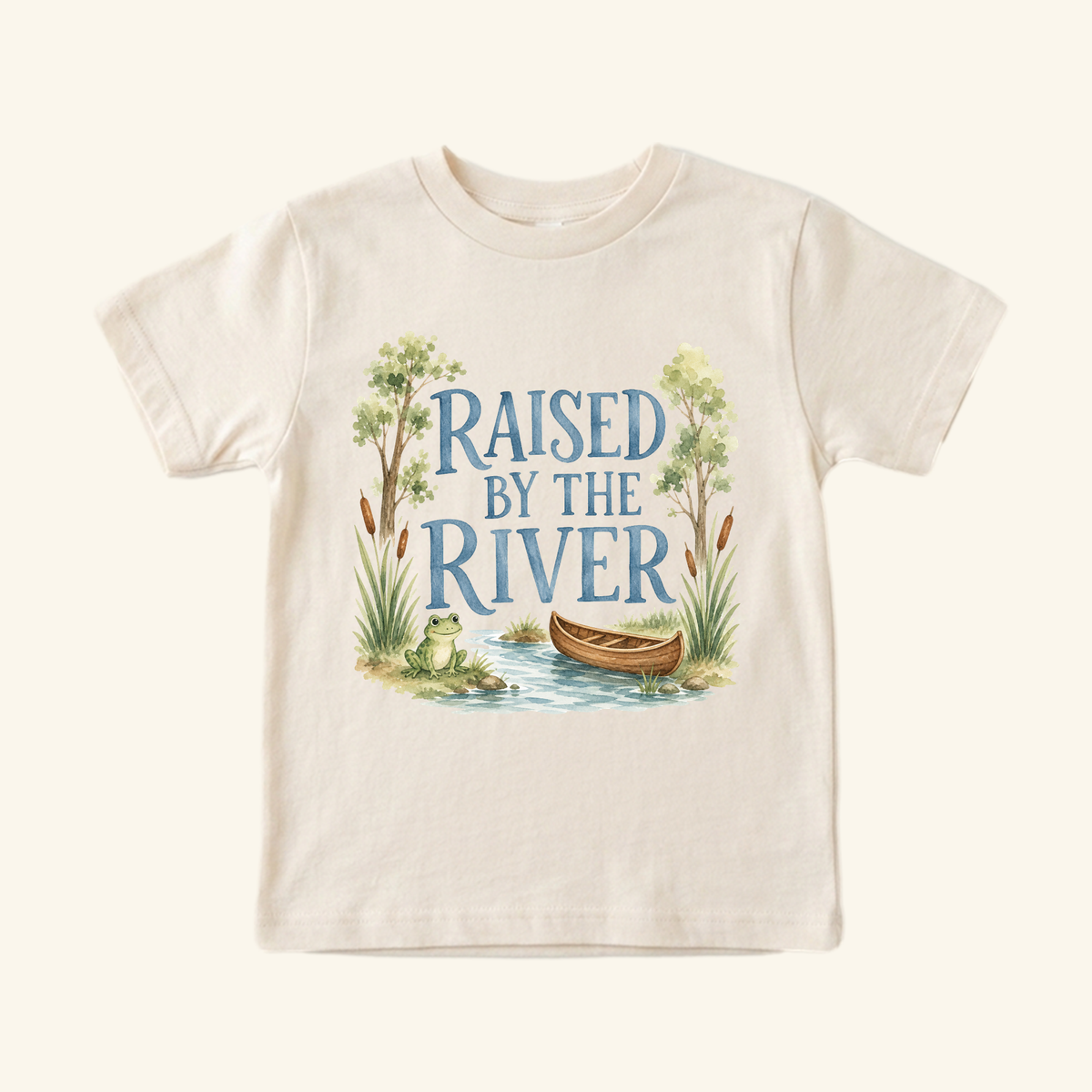 Light-colored Raised by the River Toddler Shirt – Canoe & Frog Outdoor Tee featuring a watercolor river scene with a frog and a canoe, printed with the text RAISED BY THE RIVER.