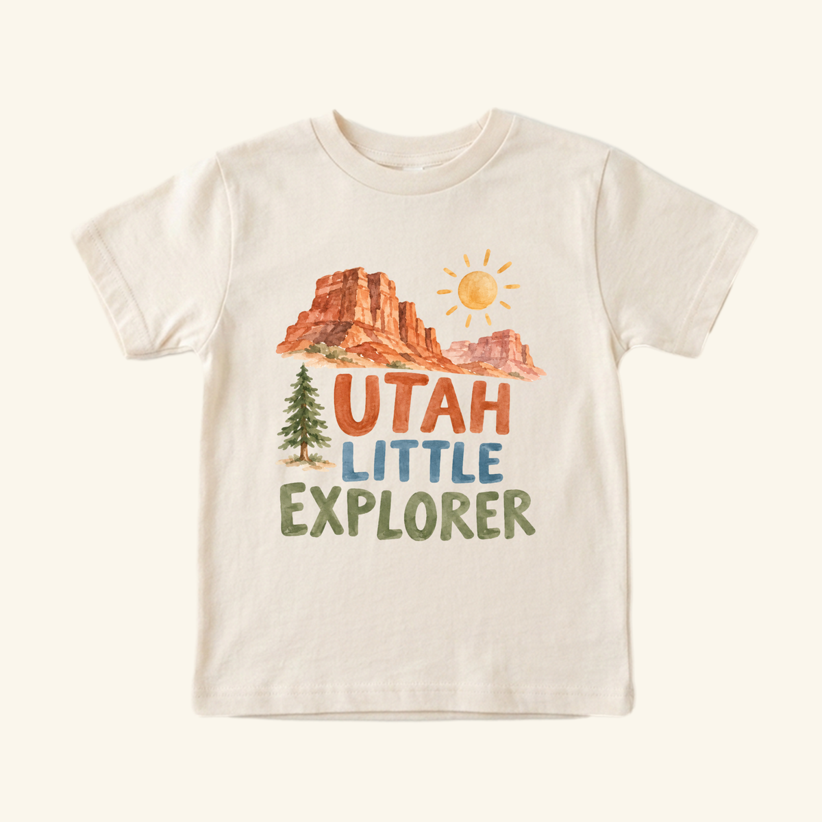 Cream-colored Utah Toddler Shirt – Little Explorer Red Rock Desert Tee featuring a watercolor red rock desert landscape, a pine tree, a sun, and the text Utah Little Explorer printed on the chest.
