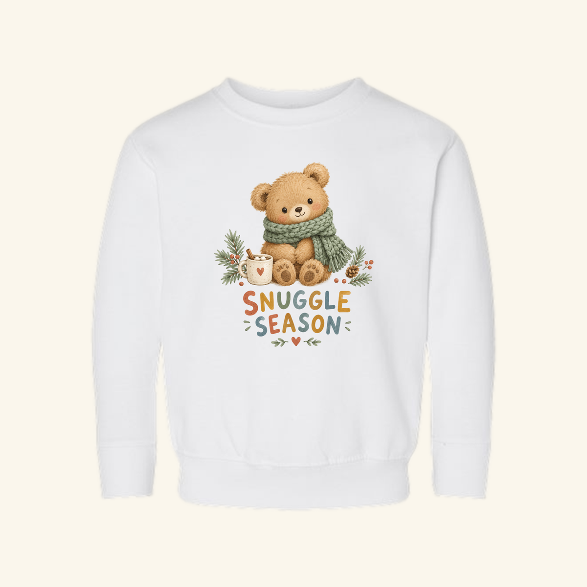 White Snuggle Season Toddler Sweatshirt – Cozy Winter Teddy Bear Pullover featuring an illustration of a teddy bear wearing a green scarf next to a mug, with the text Snuggle Season below.