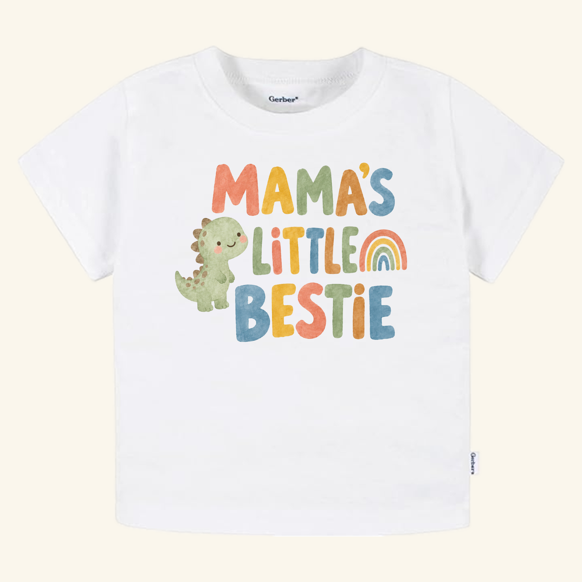 White Toodleroos Mama’s Little Bestie Toddler Shirt featuring a cartoon dinosaur, a rainbow, and the text Mama’s Little Bestie in multicolored lettering.