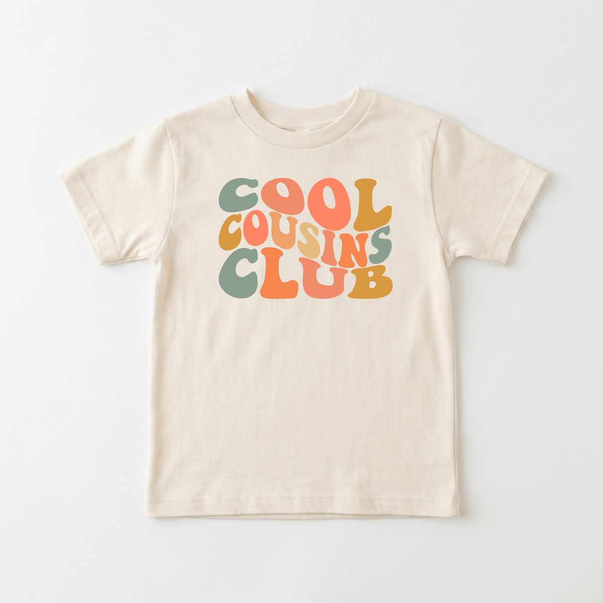 The Toodleroos Cool Cousins Club Toddler Shirt – Retro Family Tee features bold, colorful bubble letters in green, orange, and mustard spelling out COOL COUSINS CLUB on a beige tee—perfect for matching cousin outfits or a fun family reunion look.