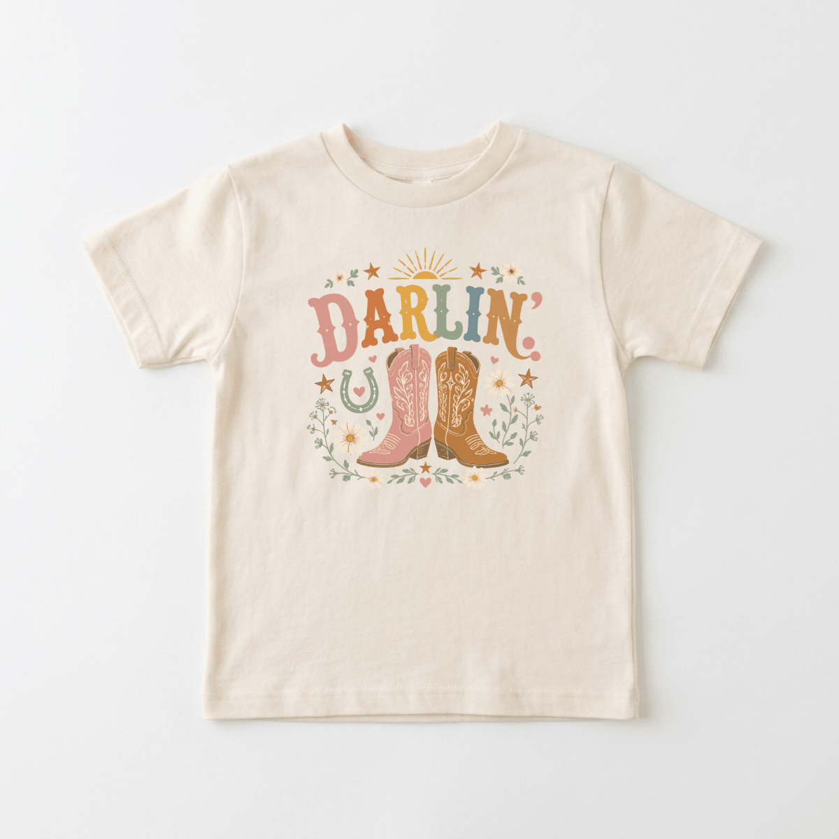 The Toodleroos Toddler Cowgirl Shirt – Darlin’ Western Cowboy Boots Short-Sleeve Tee features “Darlin” above two pink cowboy boots, surrounded by stars, a horseshoe, and floral accents. This colorful tee showcases a western, country-inspired design—perfect for adventurous little ones who love cowgirl style.