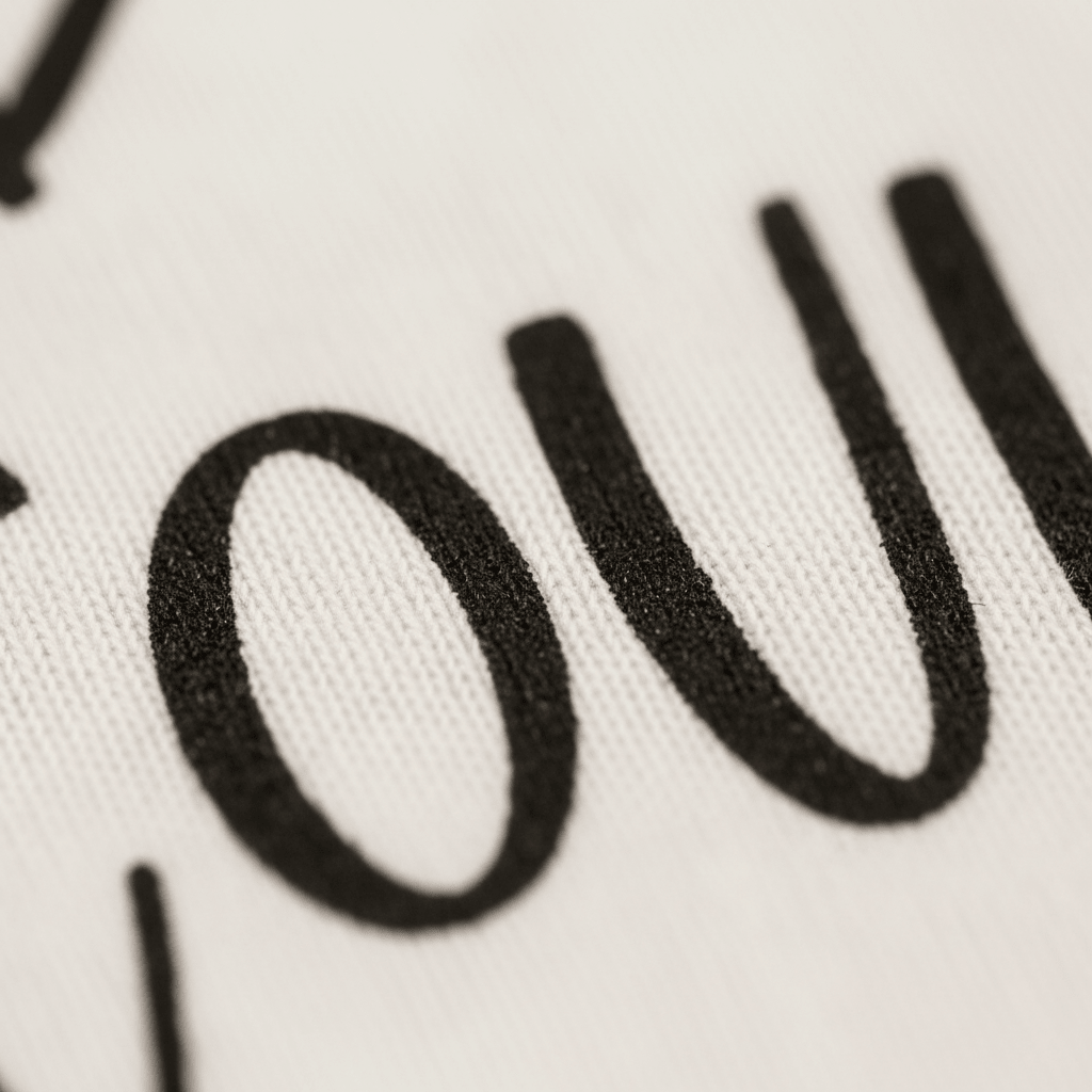 Close-up of bold, black serif text reading “ou” printed on white fabric, highlighting the detailed texture beneath the ink. This Toodleroos “Grandpa Told Me I Could Toddler Shirt – Funny Family Tee” design is perfect for family reunions or as a hilarious Grandpa toddler shirt.
