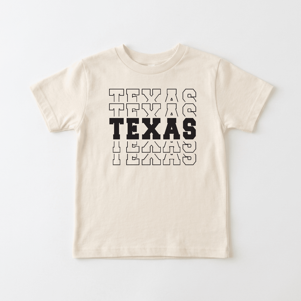 The Texas Varsity Kids Shirt – State Pride Tee by Toodleroos features a beige design with the word “TEXAS” printed five times in a stacked layout. The center TEXAS is bold and black, while the others are outlined, creating a fun varsity style that’s perfect for showing off your child’s hometown pride.