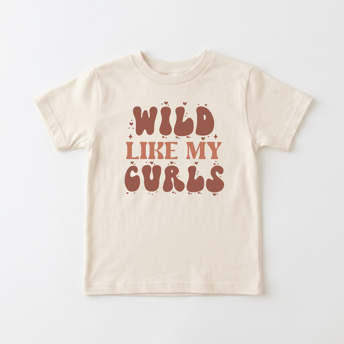 The Wild Like My Curls Kids Shirt – Boho Retro Tee by Toodleroos features bold brown text in a playful font that reads “WILD LIKE MY CURLS,” accented with charming little hearts and stars on a beige background—this retro kids shirt is perfect for free-spirited little ones and celebrates the joy of curly hair.