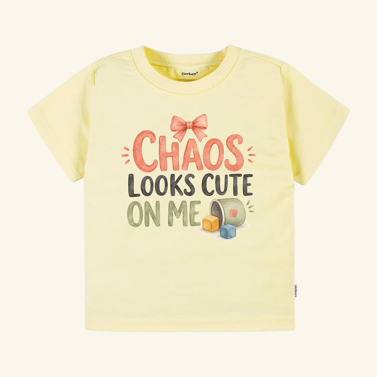 Pale yellow Chaos Looks Cute on Me Toddler Shirt with a pink bow and the text Chaos Looks Cute on Me above colorful toy blocks.
