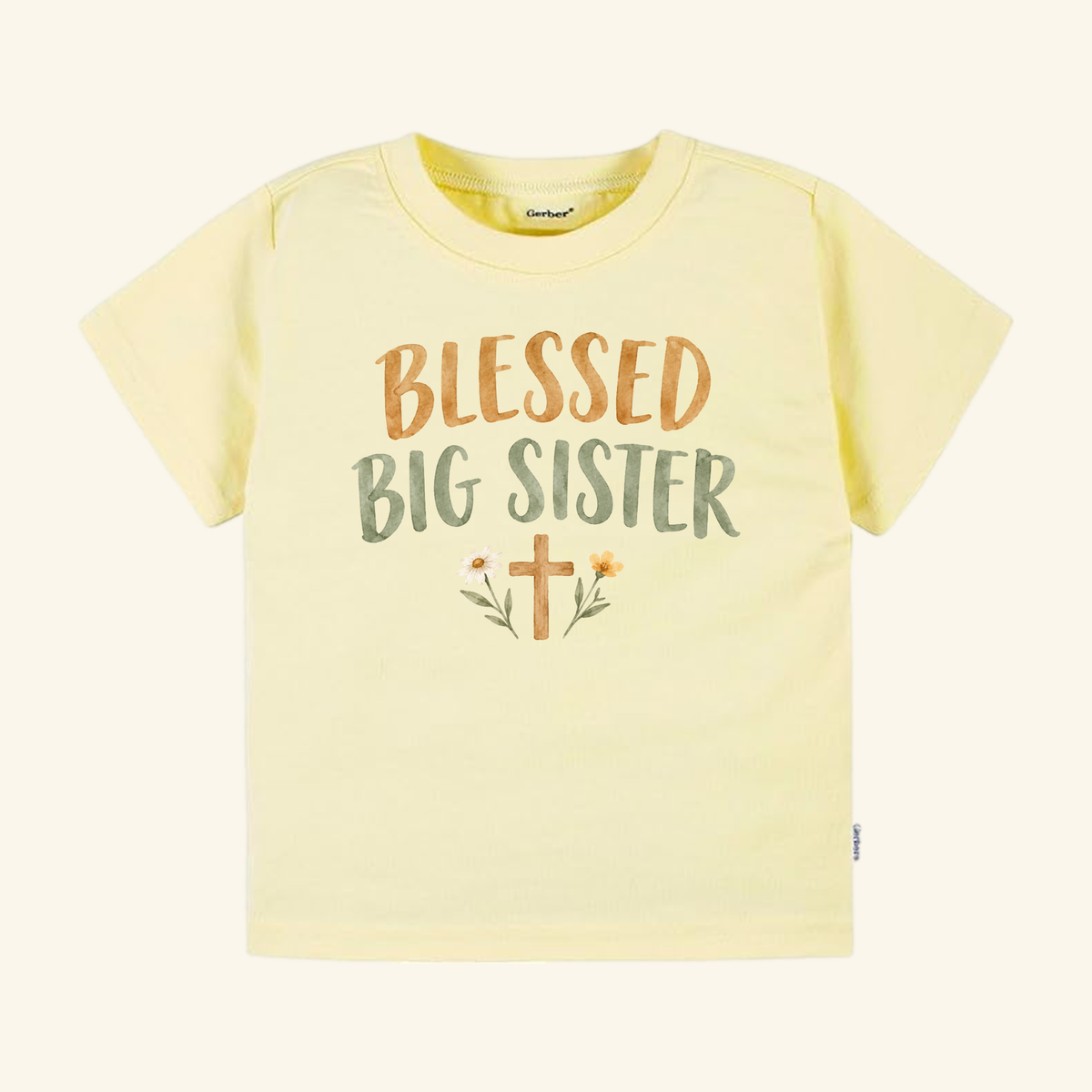 Light yellow Toodleroos Blessed Big Sister Toddler Shirt with the text BLESSED BIG SISTER in brown and green, featuring a floral cross graphic at the center.