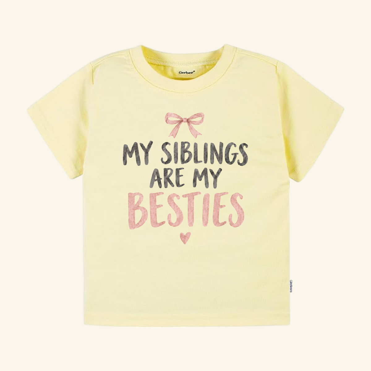 Pale yellow My Siblings Are My Besties Toddler Shirt – Pink Bow Sibling Tee featuring a pink bow graphic and the text MY SIBLINGS ARE MY BESTIES in dark grey and pink letters.