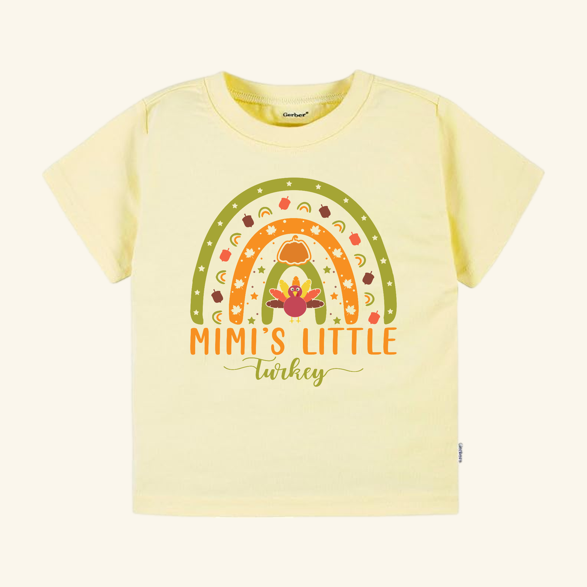 Pale yellow Mimi’s Little Turkey Toddler Shirt featuring a rainbow graphic with a turkey, pumpkin, and autumn leaf accents, and Mimi’s Little Turkey text below.