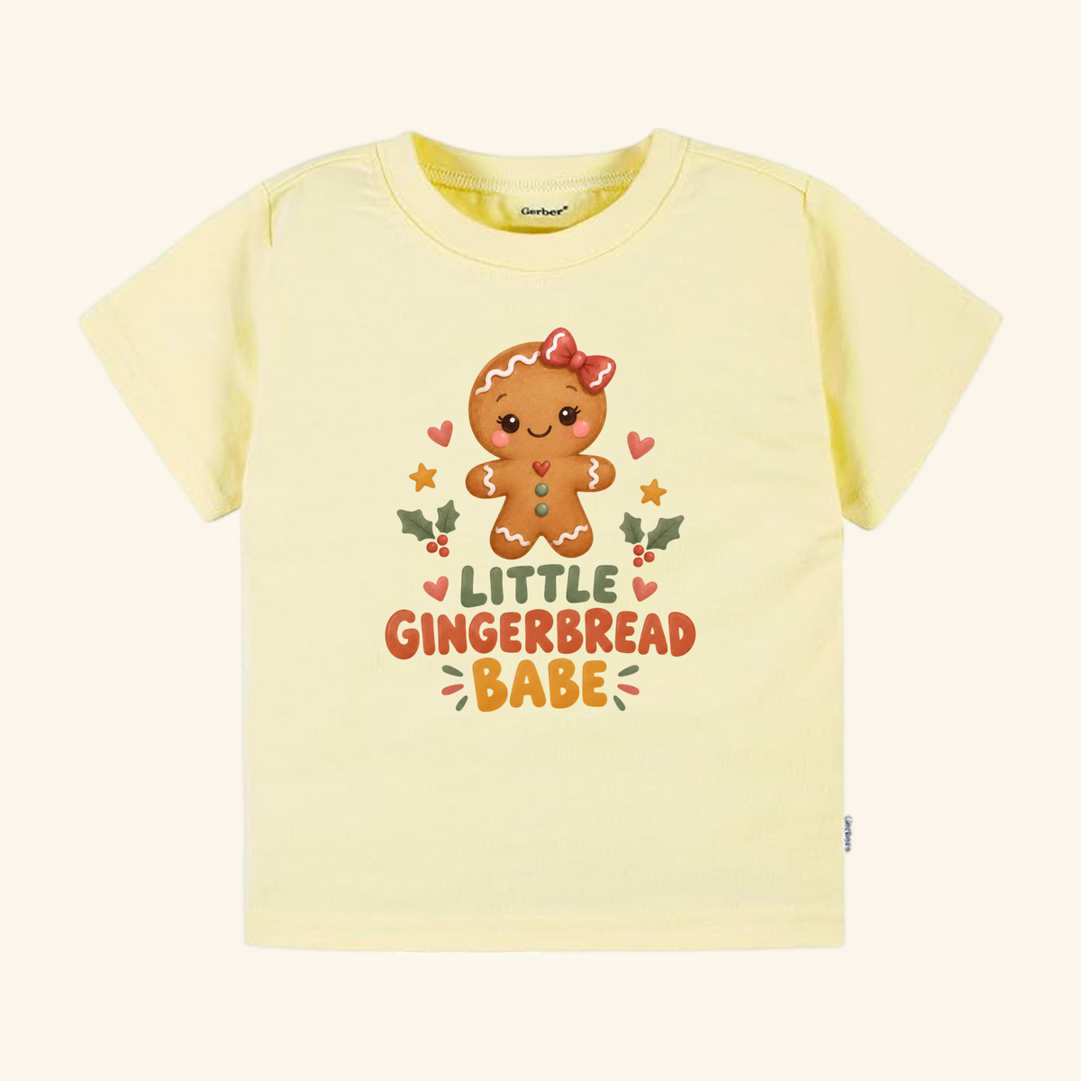 Pale yellow Little Gingerbread Babe Toddler Shirt featuring a cartoon gingerbread cookie with a red bow and the text Little Gingerbread Babe.