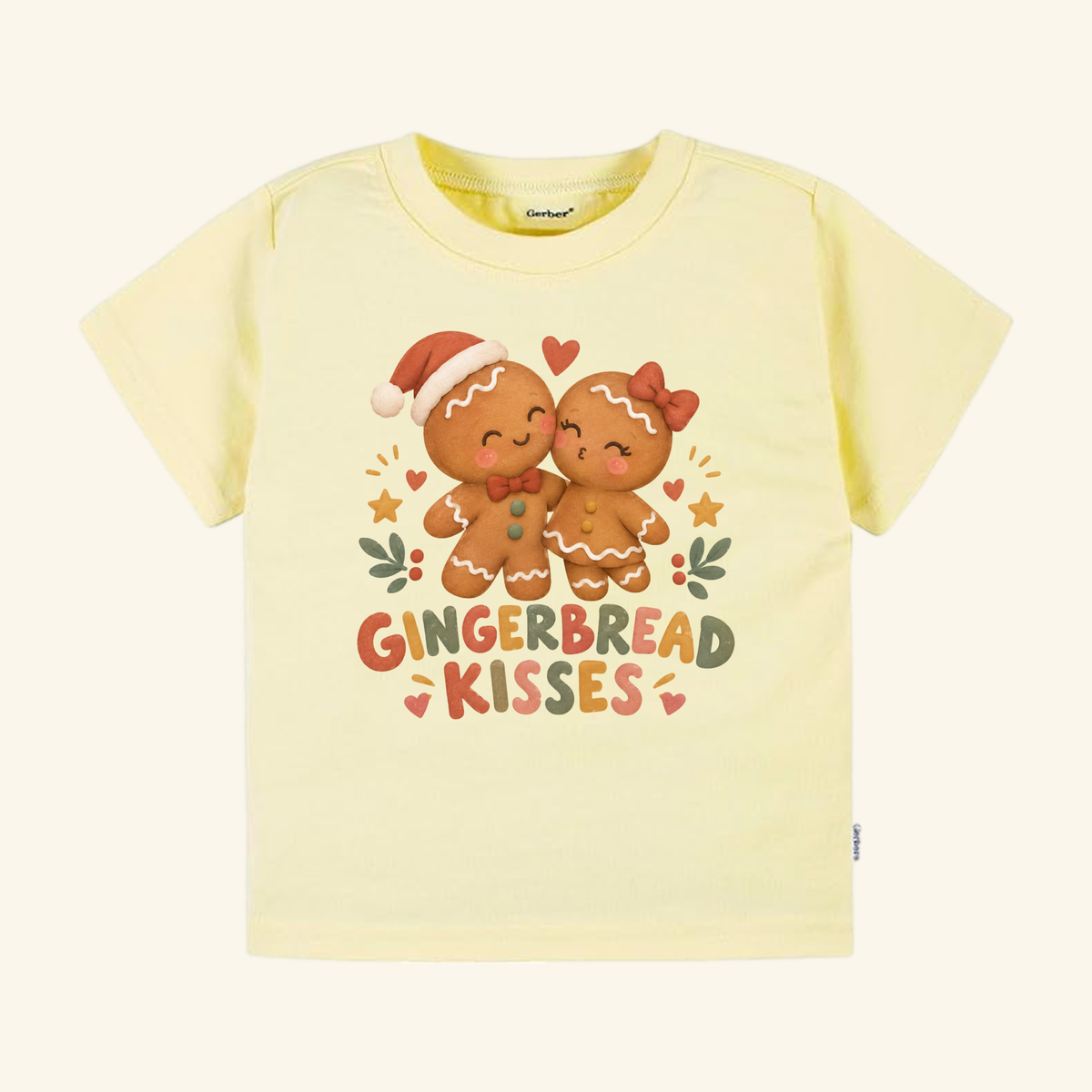 Light yellow Gingerbread Kisses Toddler Shirt featuring two gingerbread cookies kissing, surrounded by hearts and stars, with the text GINGERBREAD KISSES below this festive holiday shirt for kids.