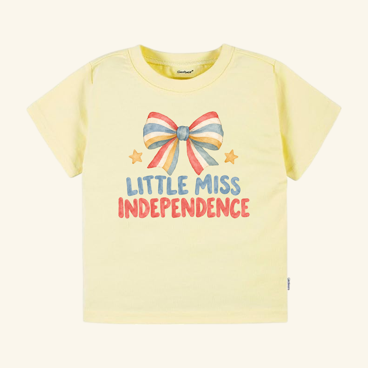 Little Miss Independence Toddler Shirt – Patriotic Bow Tee in pale yellow with a watercolor graphic of a red, white, and blue striped bow, two small stars, and the text Little Miss Independence.