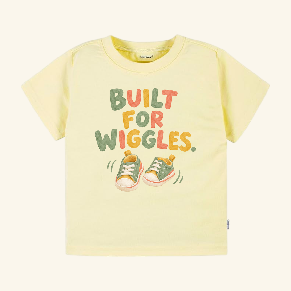 Pale yellow Built for Wiggles Toddler Shirt with the text BUILT FOR WIGGLES in colorful letters above an illustration of two small sneakers.