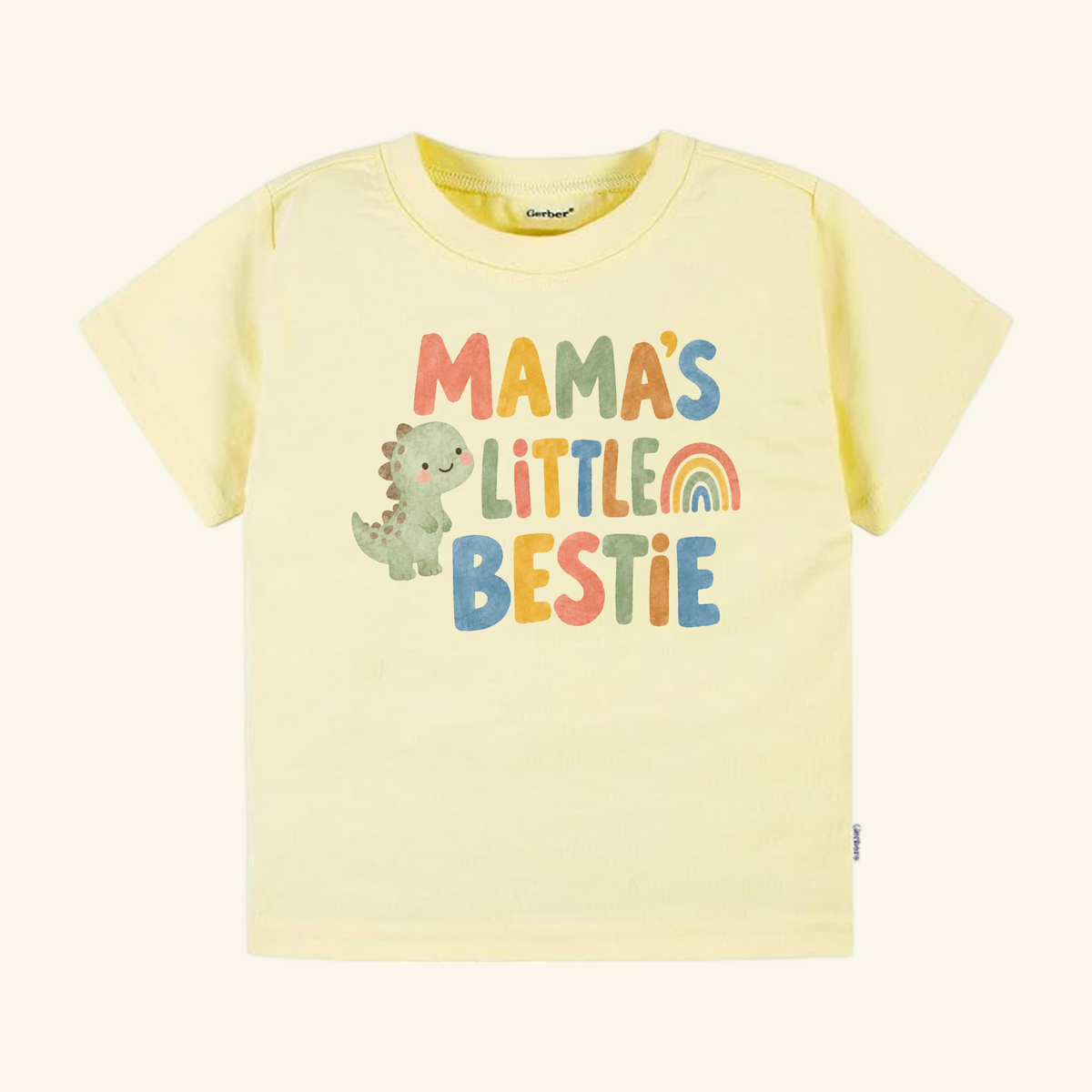 Pale yellow Mama’s Little Bestie Toddler Shirt featuring a green dinosaur, a rainbow, and the text Mama’s Little Bestie.