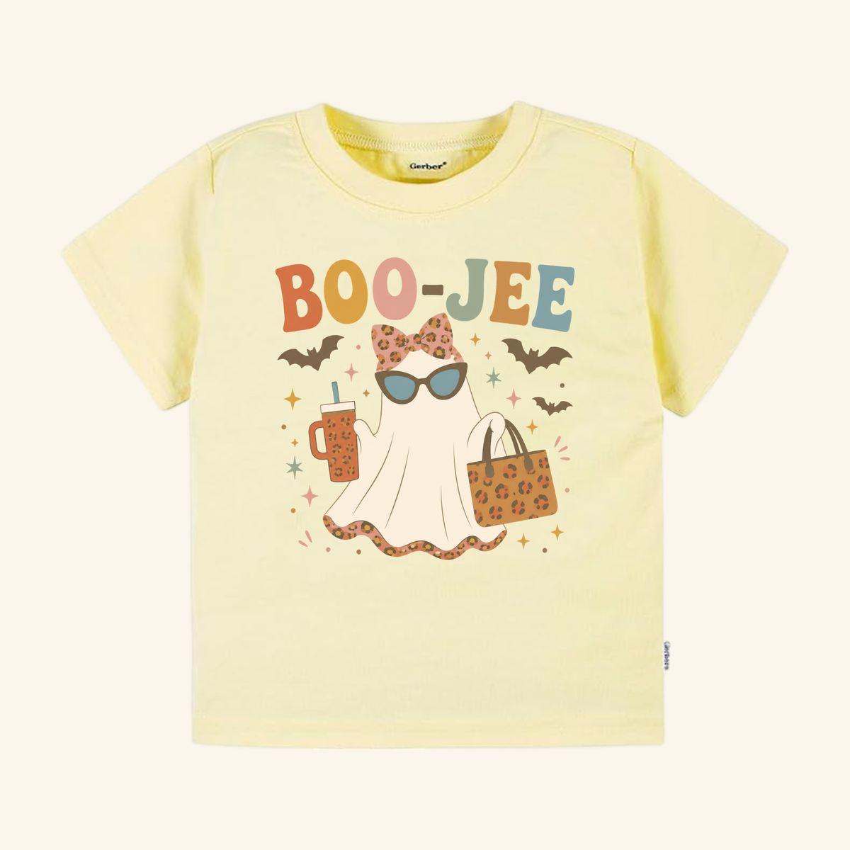 Pale yellow Toddler Girl Halloween Shirt – Boo-Jee Ghost Short-Sleeve Tee featuring a graphic of a ghost wearing sunglasses and a leopard-print bow, holding a drink and a tote bag.