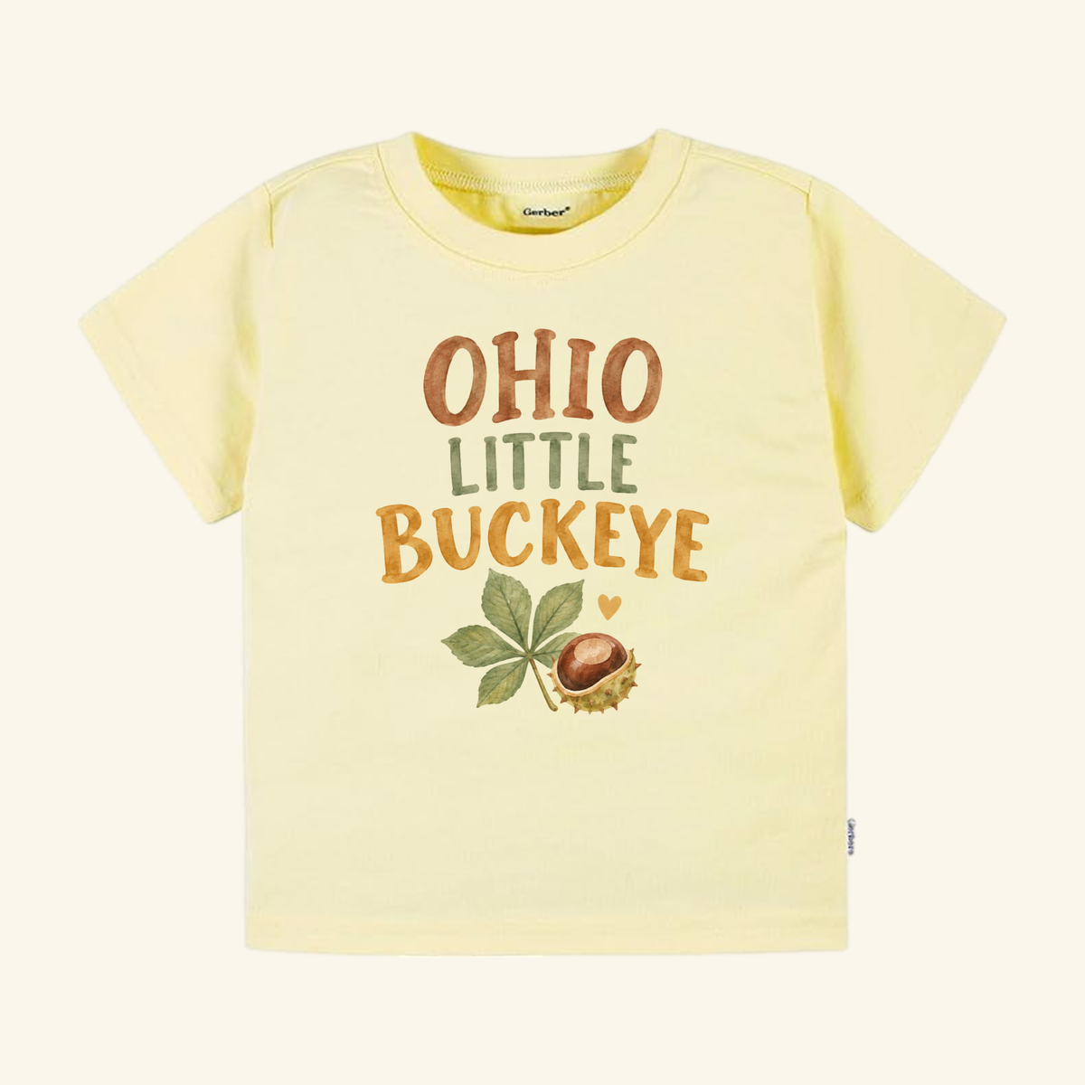 Pale yellow Toodleroos Ohio Toddler Shirt – Little Buckeye Watercolor Nut & Leaf Tee with the text LITTLE BUCKEYE in brown and green, featuring a watercolor illustration of a buckeye nut and leaf below.