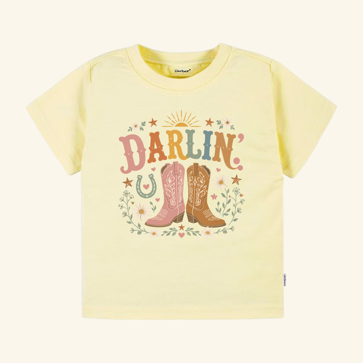 Pale yellow Toddler Cowgirl Shirt – Darlin’ Western Cowboy Boots Short-Sleeve Tee featuring the text DARLIN above two illustrated western boots, surrounded by flowers, stars, and a horseshoe.
