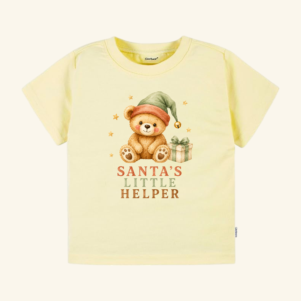 Pale yellow short-sleeve Santa’s Little Helper Toddler Shirt – Teddy Bear Christmas Tee featuring a teddy bear wearing a holiday elf hat next to a wrapped gift.