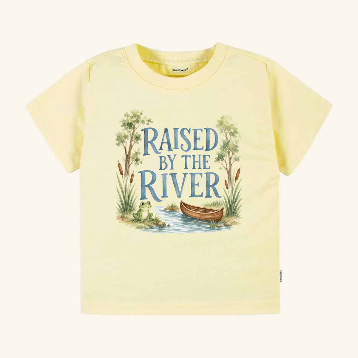 Light yellow Raised by the River Toddler Shirt – Canoe & Frog Outdoor Tee featuring a watercolor illustration of a frog in a canoe on a river with the text Raised by the River.