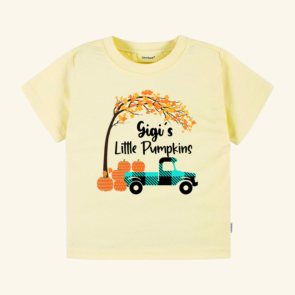 Pale yellow Gigi’s Little Pumpkins Toddler Shirt featuring a graphic of a plaid truck carrying pumpkins under an autumn tree.