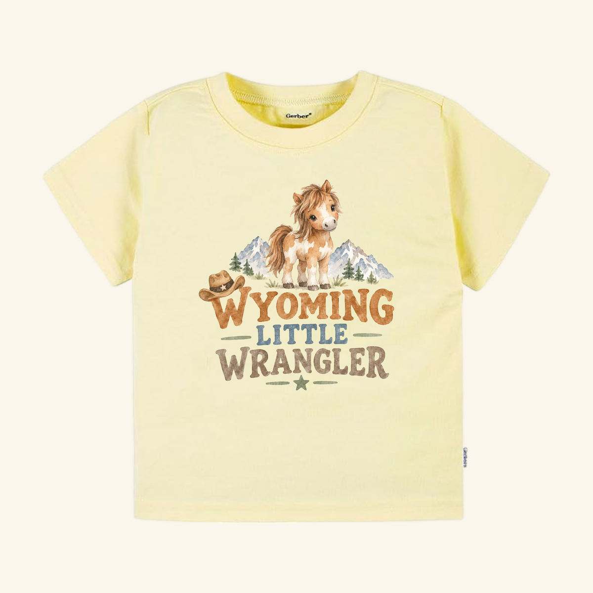 Pale yellow Wyoming Toddler Shirt – Little Wrangler Western Pony Tee featuring a watercolor illustration of a pony, mountains, and a cowboy hat with the text WYOMING LITTLE WRANGLER.