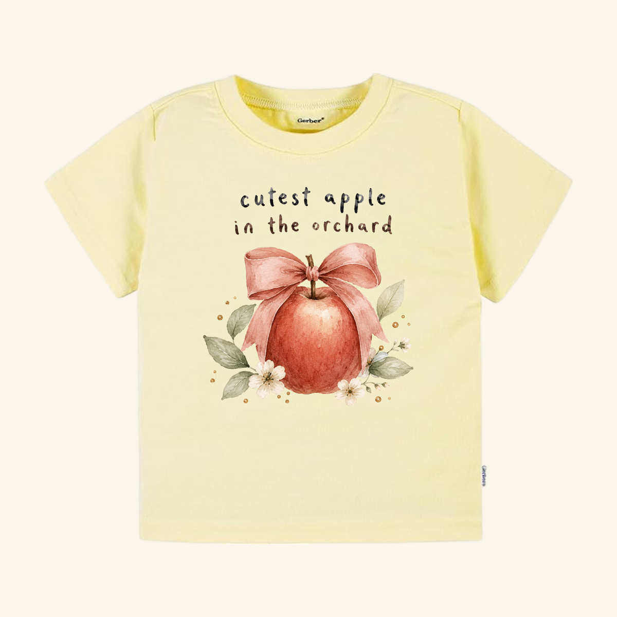 Pale yellow Toodleroos Cutest Apple in the Orchard Toddler Shirt – Fall Apple Bow Tee featuring an apple with a bow, surrounded by leaves and flowers with the text cutest apple in the orchard.