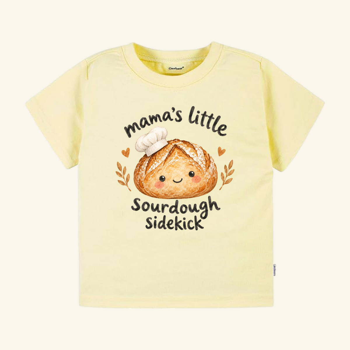 Pale yellow Mama’s Little Sourdough Sidekick Toddler Shirt featuring a smiling loaf of bread in a chef’s hat and the text mama’s little sourdough sidekick.