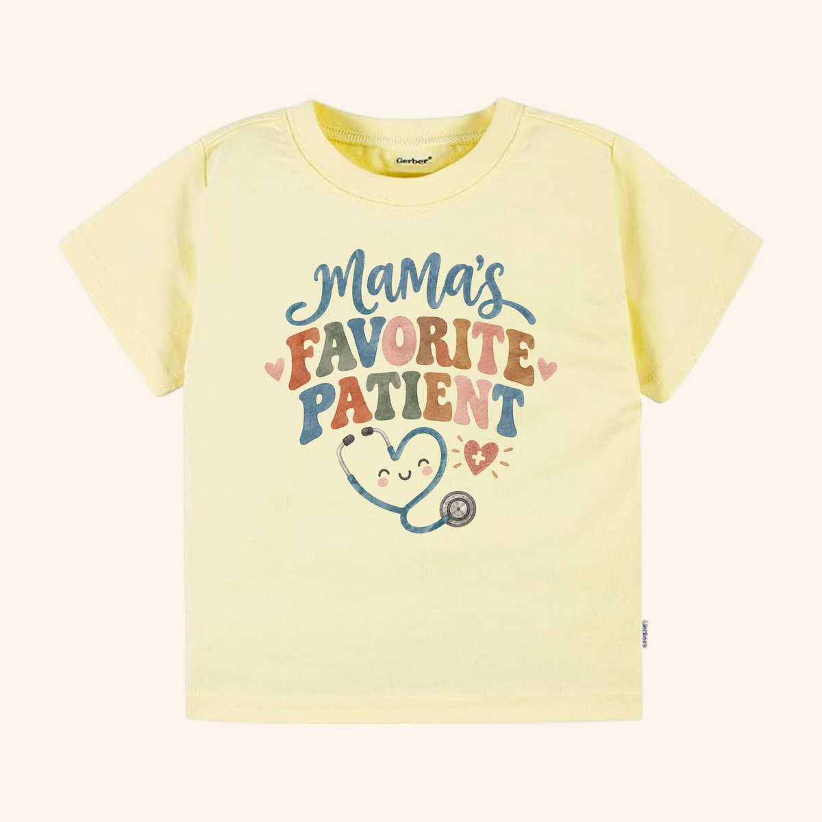 Pale yellow Mama’s Favorite Patient Toddler Shirt with the text Mamas Favorite Patient above a graphic of a smiling stethoscope shaped like a heart.