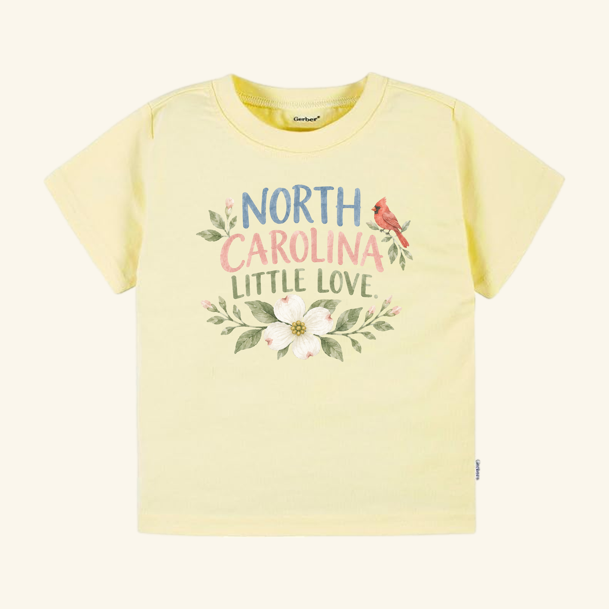 North Carolina Toddler Shirt – Little Love Dogwood & Cardinal Tee in pale yellow, featuring a colorful North Carolina Little Love graphic with a cardinal and a dogwood flower.