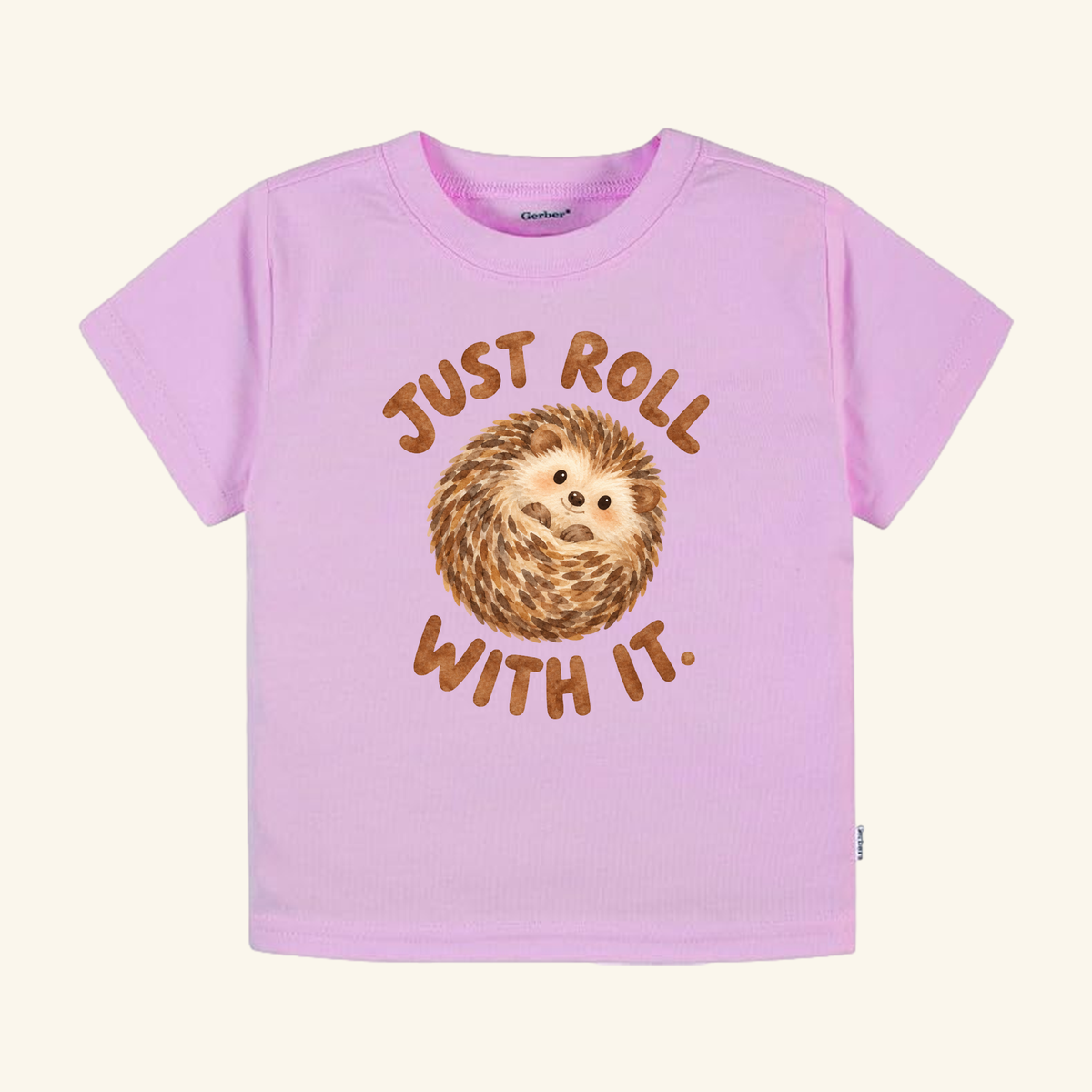 Light pink Just Roll With It Toddler Shirt – Cute Hedgehog Tee featuring a cartoon hedgehog curled into a ball, surrounded by the brown text Just roll with it.