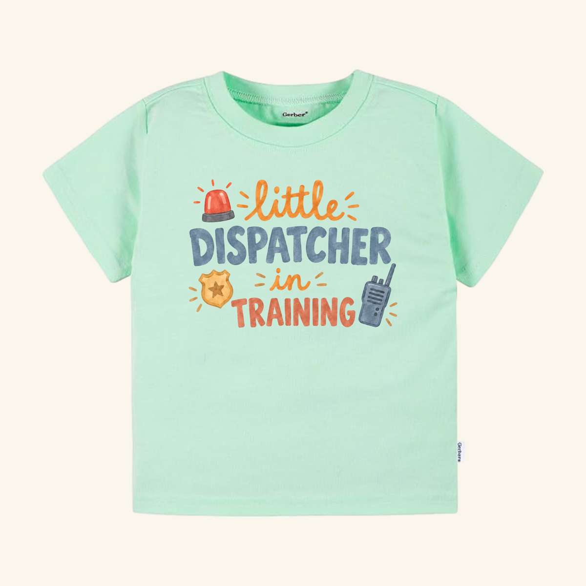 Light green Toodleroos Little Dispatcher in Training Toddler Shirt featuring little DISPATCHER in TRAINING text surrounded by a red siren, gold badge, and walkie-talkie.