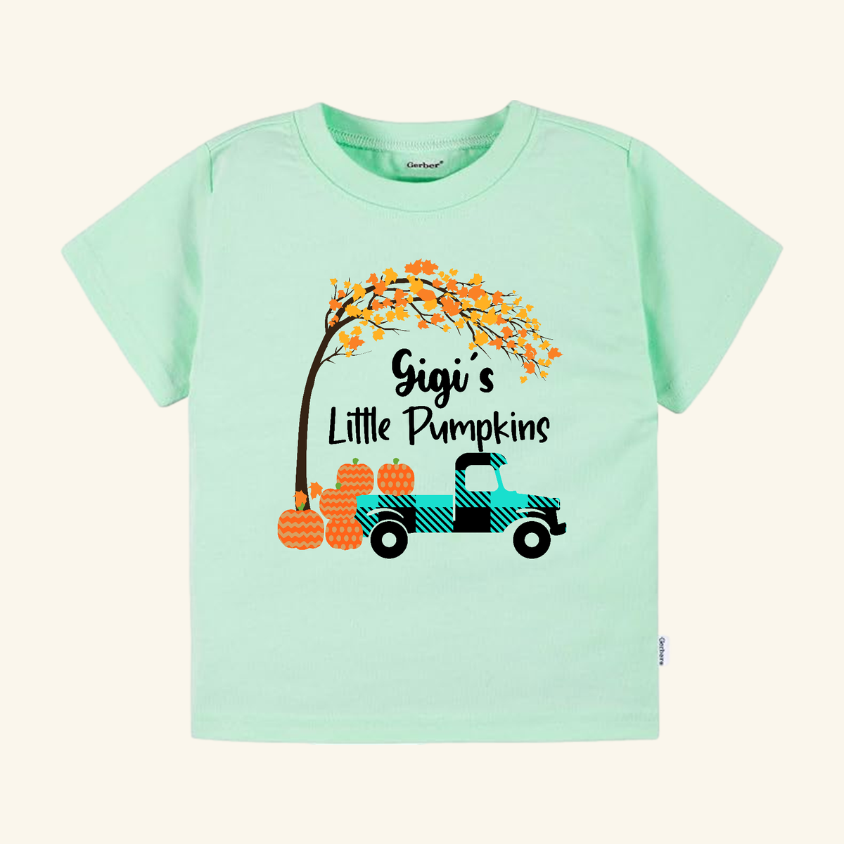 Gigi’s Little Pumpkins Toddler Shirt features a light green tee with a teal plaid truck, orange patterned pumpkins, and a tree with autumn leaves.