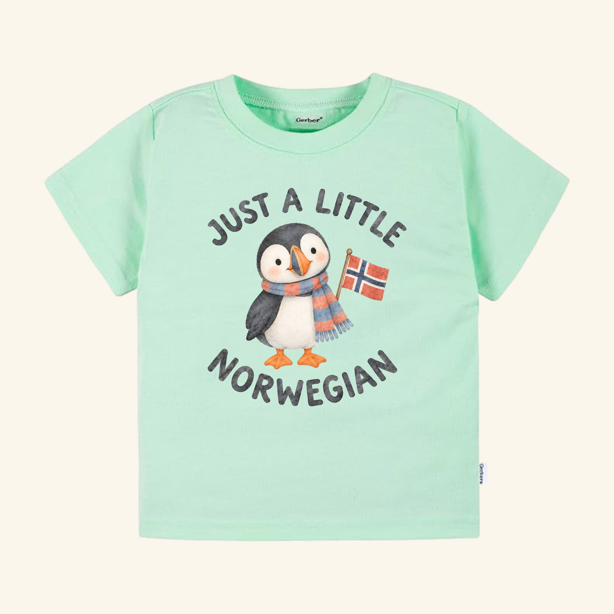 Just a Little Norwegian Toddler Shirt – Cute Puffin Norway Flag Tee featuring a light green tee with a cartoon puffin wearing a striped scarf and holding a Norwegian flag, surrounded by the text Just a little Norwegian.