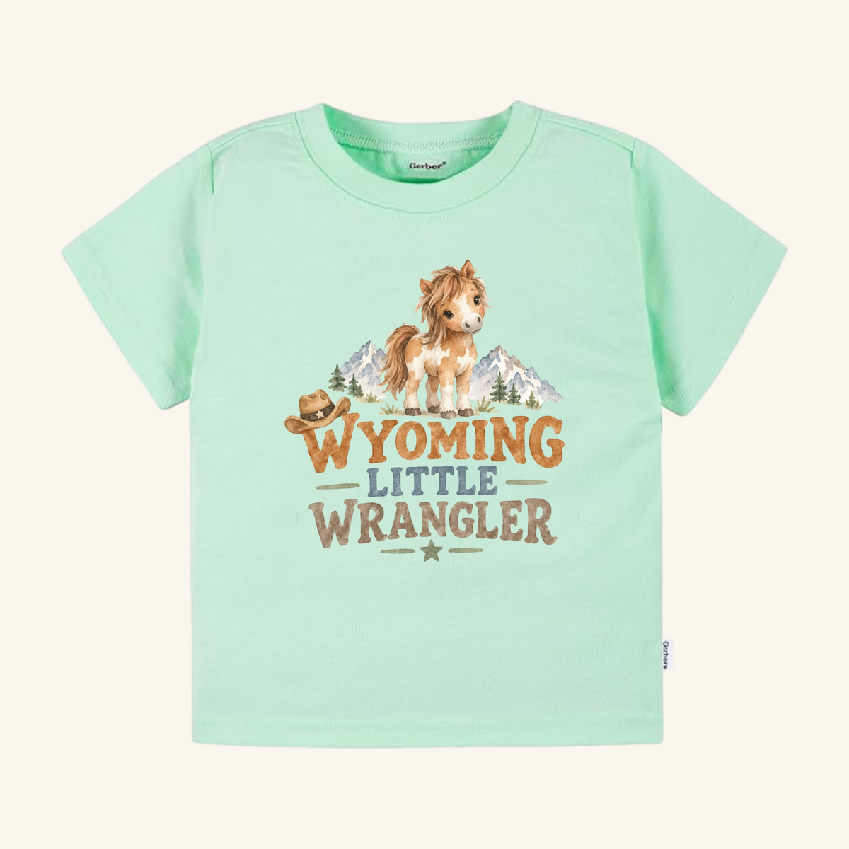 Light green Wyoming Toddler Shirt – Little Wrangler Western Pony Tee featuring a watercolor illustration of a pony, mountains, and a cowboy hat with the text WYOMING LITTLE WRANGLER.