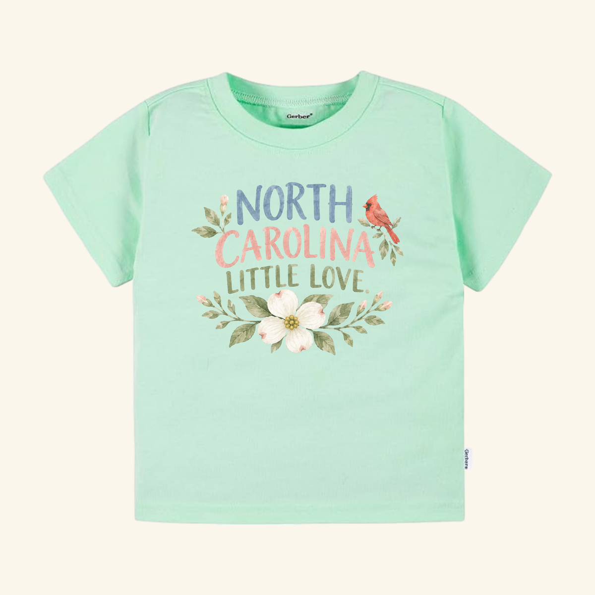 Mint green North Carolina Toddler Shirt – Little Love Dogwood & Cardinal Tee featuring a North Carolina cardinal and dogwood flower graphic with the text NORTH CAROLINA LITTLE LOVE.