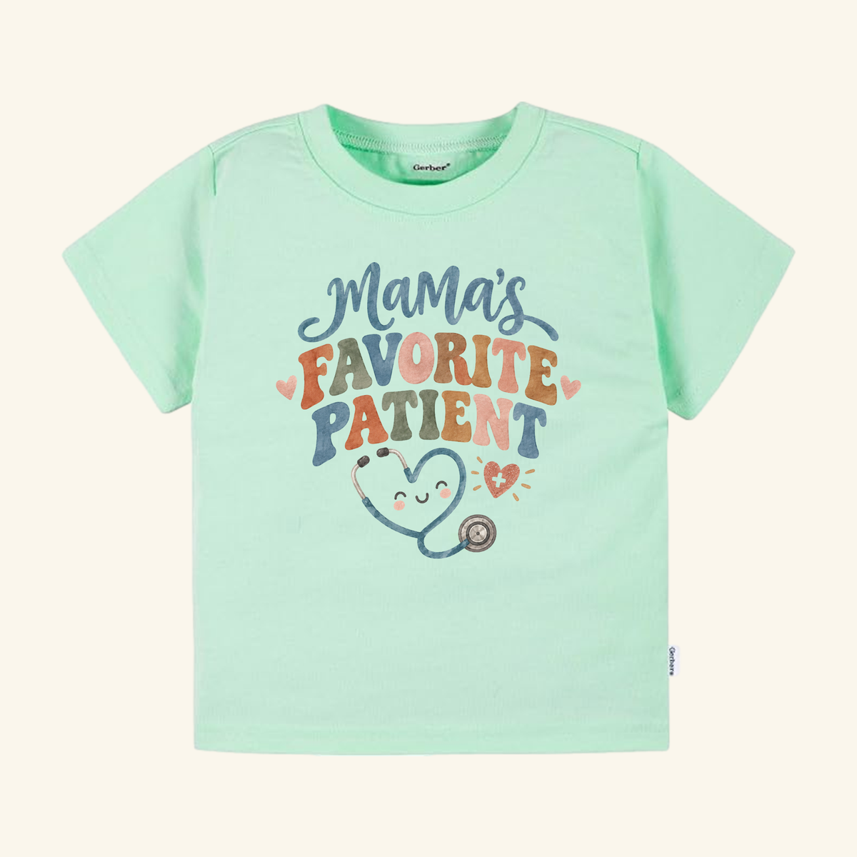 Mint green Mama’s Favorite Patient Toddler Shirt featuring a smiling stethoscope illustration that forms a heart.