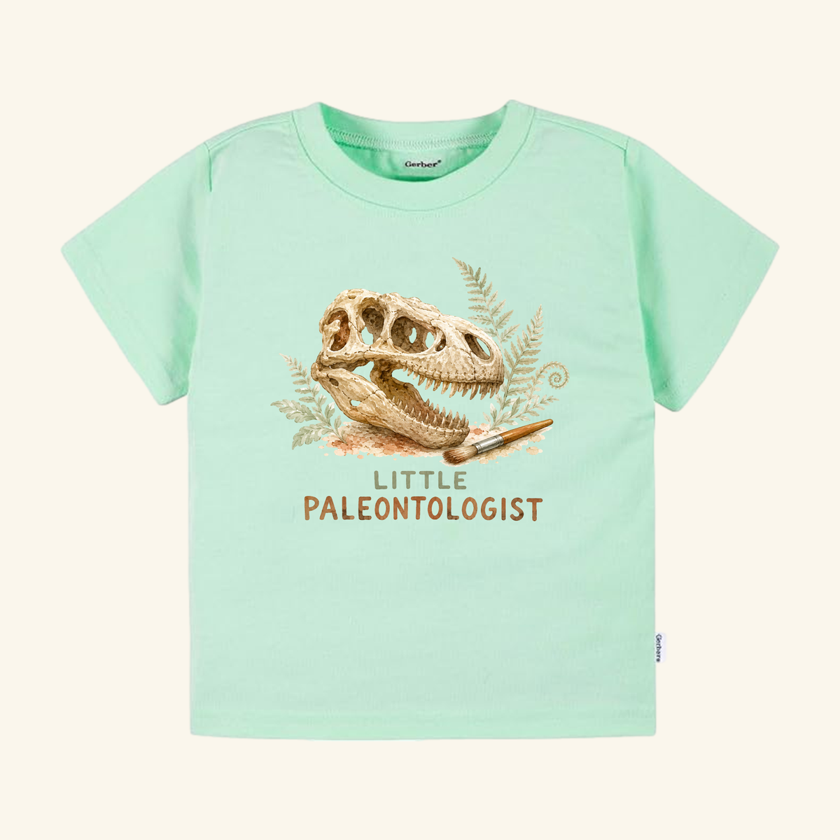 Light green Little Paleontologist Toddler Shirt – T. Rex Fossil Dinosaur Tee featuring a T. rex fossil skull graphic, a small paintbrush, fern leaves, and the text Little Paleontologist.