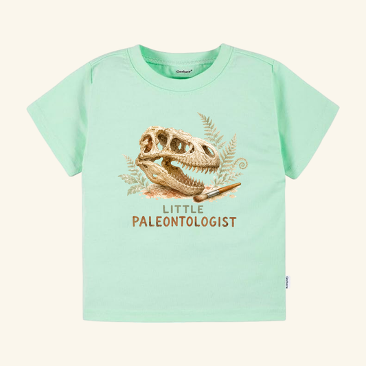 Light green Little Paleontologist Toddler Shirt – T. Rex Fossil Dinosaur Tee featuring a T. rex fossil skull graphic, a small paintbrush, fern leaves, and the text Little Paleontologist.