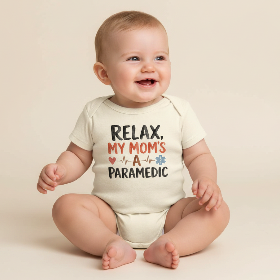 A smiling baby wearing the Toodleroos Paramedic Mom Baby Onesie – My Mom’s a Paramedic Short-Sleeve Bodysuit, featuring “Relax, my mom’s a paramedic” with heart and heartbeat graphics, sits on a light background—making this an ideal baby shower gift or a thoughtful present for any paramedic mom.