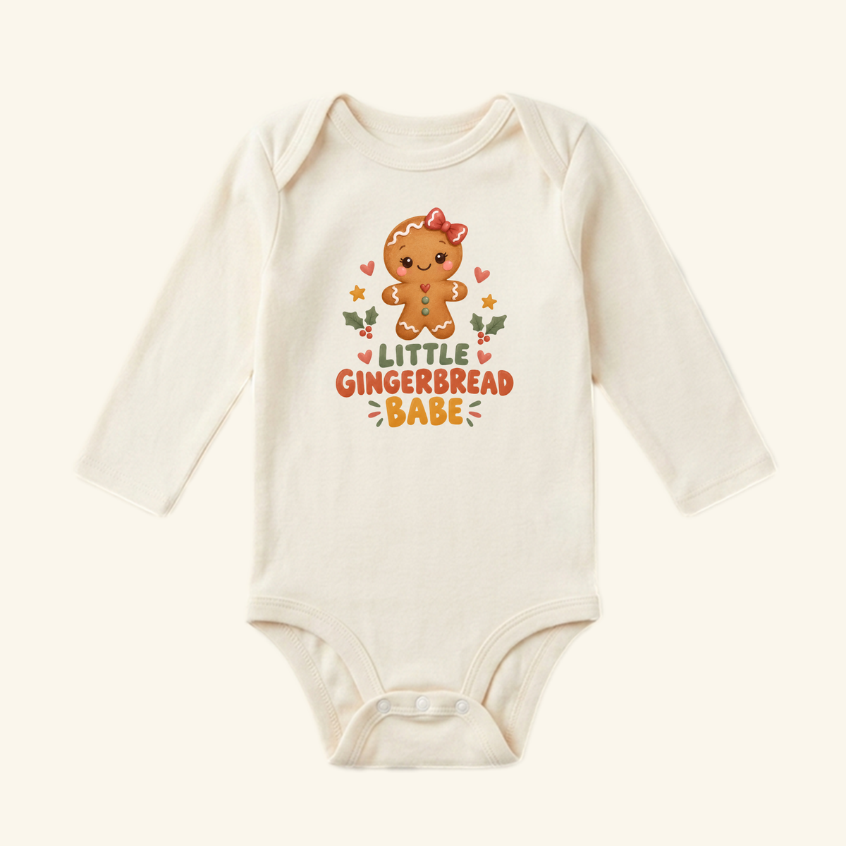 Little Gingerbread Babe Baby Onesie in cream, featuring a long-sleeved gingerbread person with a bow, holly, and stars, with the text Little Gingerbread Babe printed above.