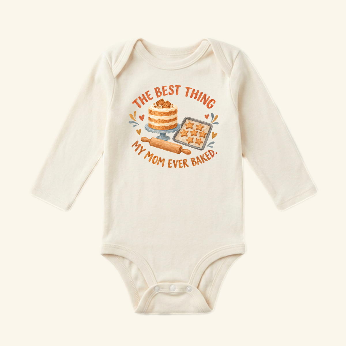 Cream-colored long-sleeve Best Thing My Mom Baked Baby Onesie – Cute Mom Baking Bodysuit featuring a cake, star-shaped cookies, a rolling pin, and the text The best thing my mom ever baked.