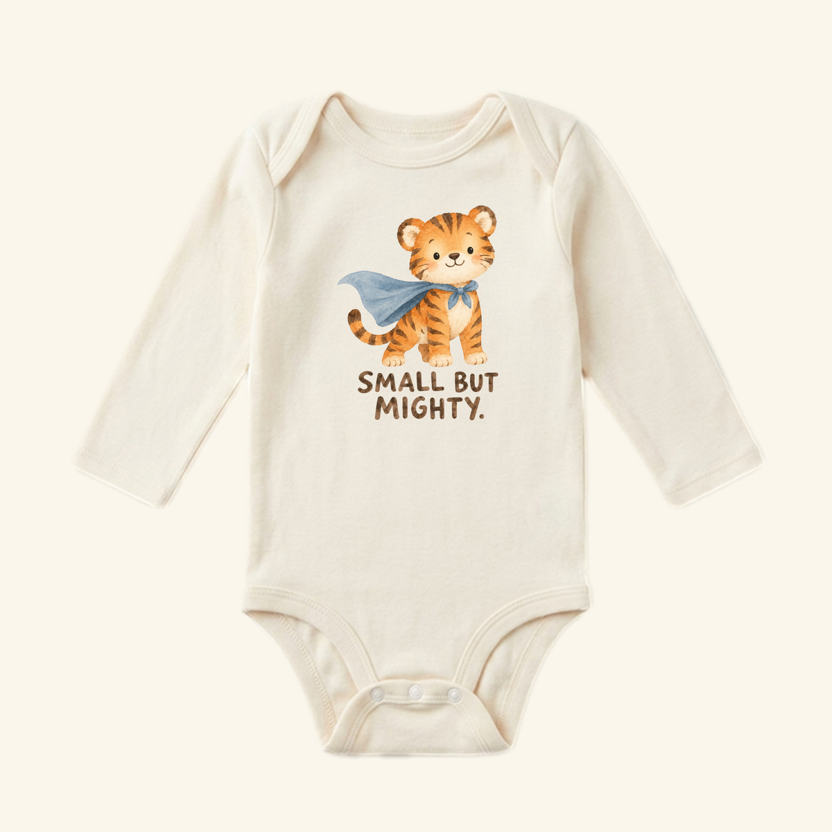 Cream-colored long-sleeve Small But Mighty Baby Onesie featuring a watercolor illustration of a tiger in a blue cape with the text SMALL BUT MIGHTY printed below the design.