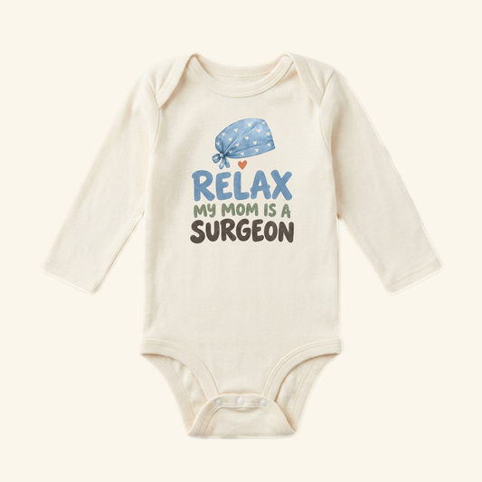 Surgeon Mom Baby Onesie – Relax My Mom Is a Surgeon Bodysuit featuring a long-sleeved white onesie with a graphic of a blue surgical cap with hearts and the text, Relax my mom is a surgeon.