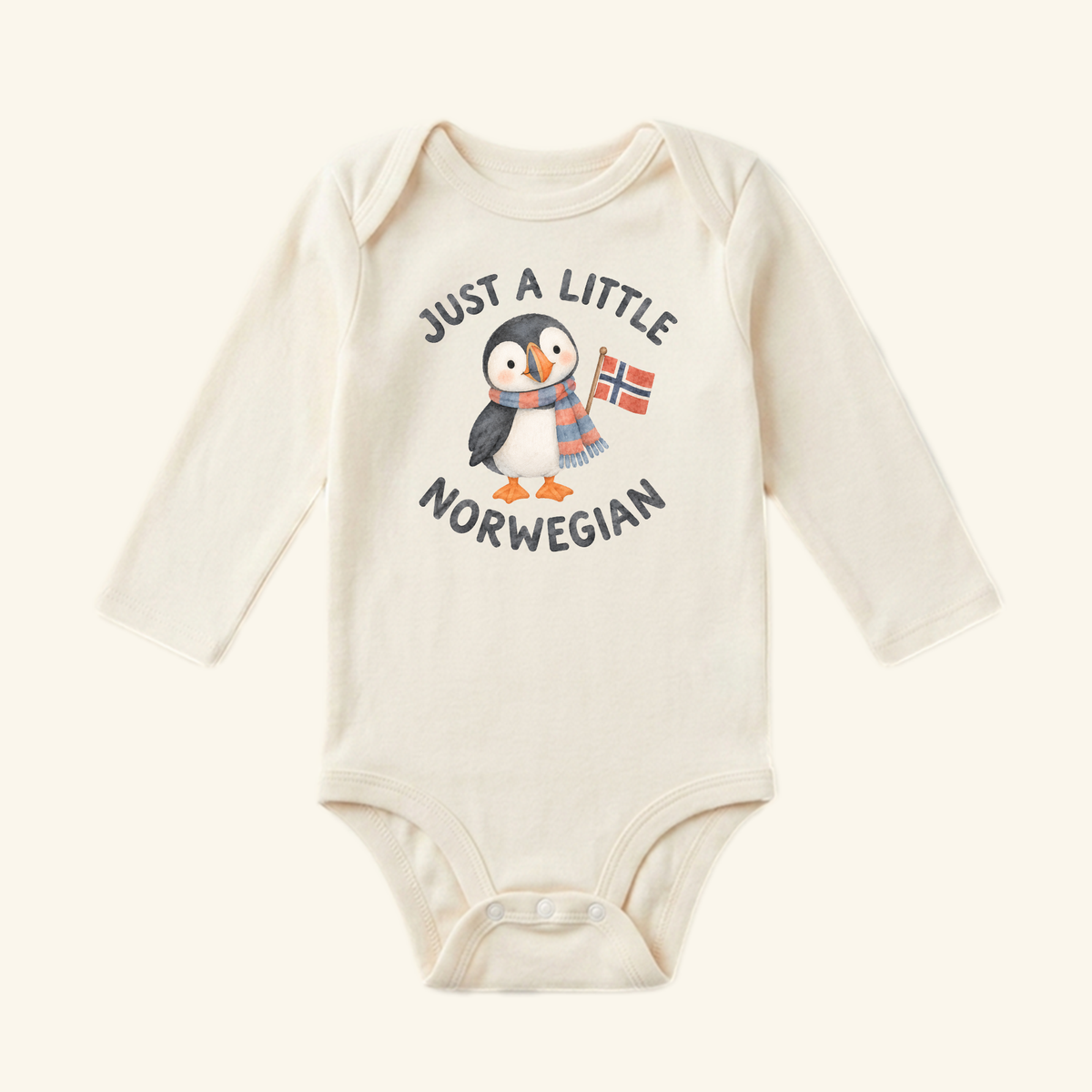 Cream-colored long-sleeve Just a Little Norwegian Baby Onesie featuring a watercolor puffin wearing a scarf, holding a Norwegian flag, and the text Just a Little Norwegian.