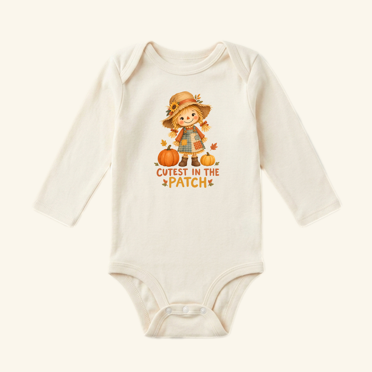 Cream-colored long-sleeve Cutest in the Patch Baby Onesie – Fall Scarecrow Girl Bodysuit featuring a scarecrow girl illustration between two pumpkins with the text Cutest in the patch below.
