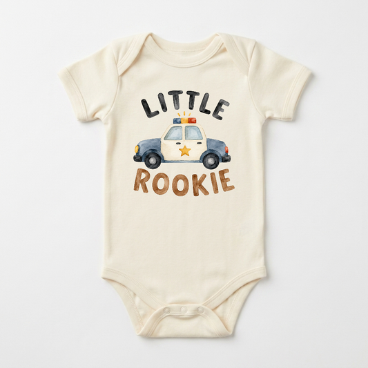 The Toodleroos Police Baby Onesie – Little Rookie Short-Sleeve Law Enforcement Bodysuit is a cream-colored baby outfit showcasing an illustrated police car with “Little Rookie” printed above and below, making it a unique and thoughtful gift for police families or anyone searching for a special law enforcement-themed bodysuit.