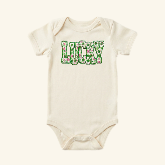 Cream-colored St. Patrick’s Day Baby Onesie – Lucky Floral Clover Bodysuit featuring a short-sleeve design and a floral clover pattern that spells out LUCKY.