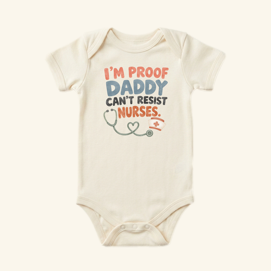 Cream-colored I’m Proof Daddy Can’t Resist Nurses Baby Onesie – Funny Nurse Mom Bodysuit printed with the text I’m proof daddy can’t resist nurses, accompanied by a stethoscope and nurse’s cap illustration.